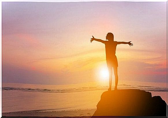 Woman on rock in front of sunrise enjoying the feeling of serotonin and dopamine