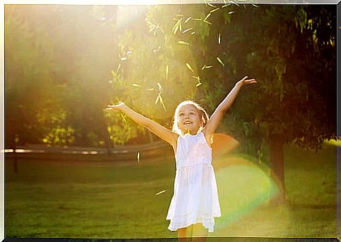 A friendly child with his arms over his head throws leaves