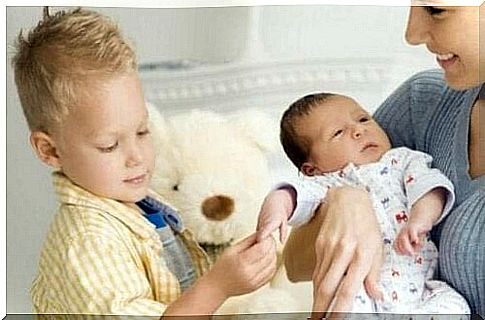 Boy playing with little brother's hand in mother's arms