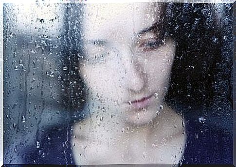 Sad woman behind wet window suffers from narcissism in a relationship