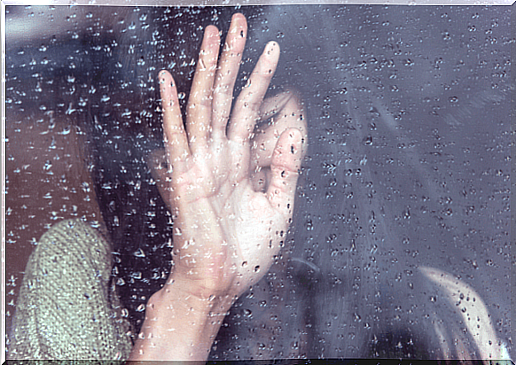 Woman puts hand up on pane with rain on