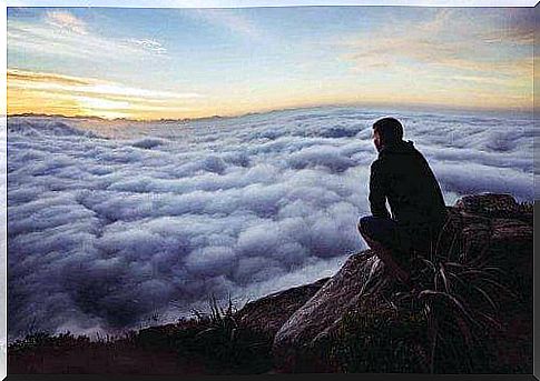 Man on rock looking at clouds from the top